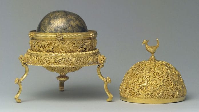 A Goa stone in a spherical, intricate gold case. The stone is gray but has a gold shimmer.