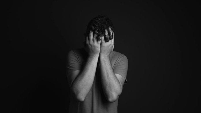 A greyscale photo of a man covering his face with his hands, representing fractured masculinity.